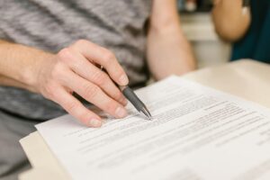 Close-up of a person's hand signing an important legal document with a pen indoors.