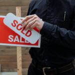 A real estate agent placing a sold sticker over a sale sign, indicating successful property deal.