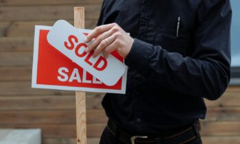 A real estate agent placing a sold sticker over a sale sign, indicating successful property deal. {{brizy_dc_image_alt entityId=